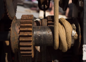 Detailed view of rusty industrial machine with gears and ropes, showcasing wear and age.