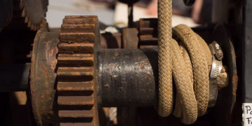 Detailed view of rusty industrial machine with gears and ropes, showcasing wear and age.