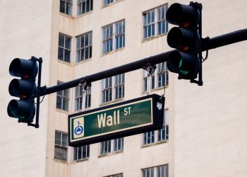 Traffic lights and Wall St sign in cityscape, symbolizing finance hub.