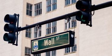 Traffic lights and Wall St sign in cityscape, symbolizing finance hub.
