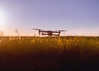 A drone flies over a field during sunset, capturing stunning aerial views.