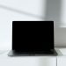 A sleek black laptop on a white desk in a minimalist setup with natural lighting.