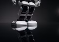 Close-up of robotic legs reflecting on a glossy surface in a studio setting.