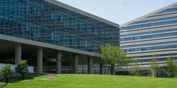 Contemporary glass office building surrounded by lush green grass in daylight.