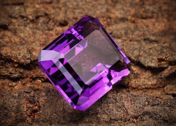 Close-up of a vibrant purple amethyst gemstone resting on a textured brown background.