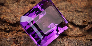 Close-up of a vibrant purple amethyst gemstone resting on a textured brown background.