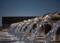 Close-up view of water flowing from industrial pipes against a clear blue sky.