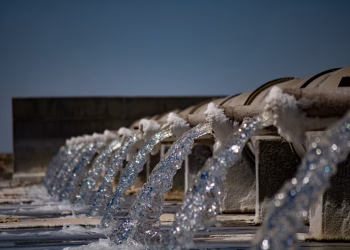 Close-up view of water flowing from industrial pipes against a clear blue sky.