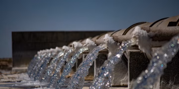 Close-up view of water flowing from industrial pipes against a clear blue sky.