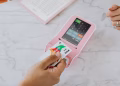 Hand using a contactless card on a pink POS terminal for a wireless transaction.