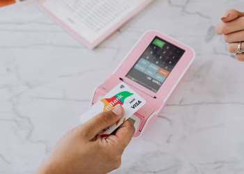 Hand using a contactless card on a pink POS terminal for a wireless transaction.