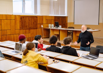 Students engaging with a professor in a university lecture hall, utilizing technology.