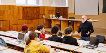 Students engaging with a professor in a university lecture hall, utilizing technology.