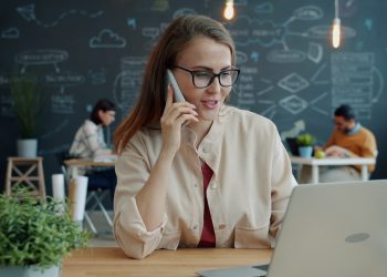 Woman talking on phone at desk with laptop
