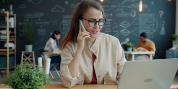 Woman talking on phone at desk with laptop