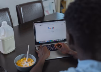 A person browsing Google on a laptop while having cereal breakfast at the table.