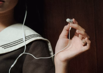 A close-up image of a hand holding earphones next to a person wearing navy attire, suggesting a relaxed mood.