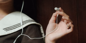 A close-up image of a hand holding earphones next to a person wearing navy attire, suggesting a relaxed mood.