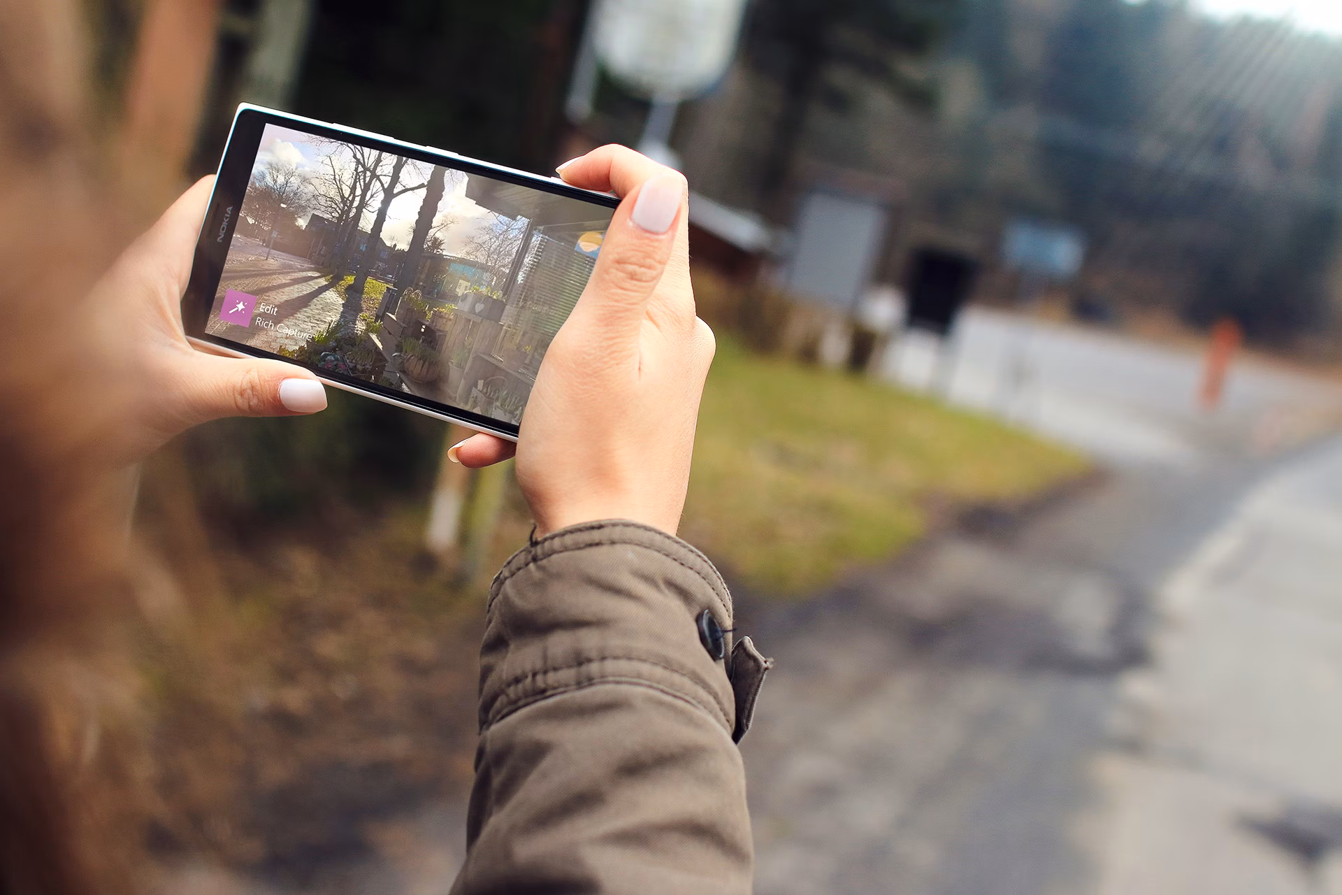Woman capturing outdoor scenery using a smartphone. Close-up of hands holding the device.