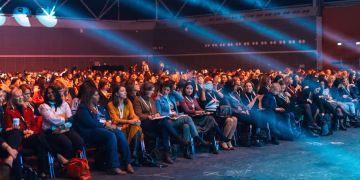 Vibrant image of a diverse audience seated in a large auditorium, highlighted by dynamic stage lighting.