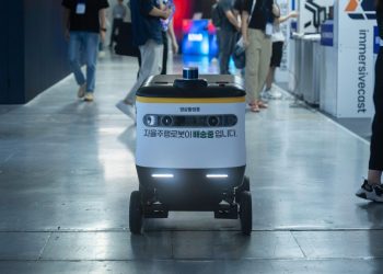 Autonomous delivery robot navigating indoors during a technology event.