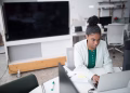 Focused woman using a laptop in a modern office setting, wearing a white blazer, working diligently.