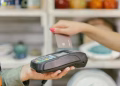 A hand using a credit card for payment at a point of sale terminal, close-up view.