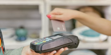 A hand using a credit card for payment at a point of sale terminal, close-up view.