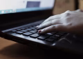 A close-up view of a person typing on a laptop keyboard indoors.