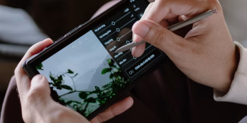 Close-up of a person editing photos on a smartphone with a stylus indoors.