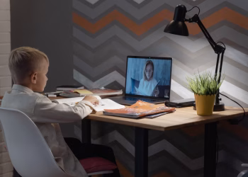 A young boy focused on a virtual class at his home desk, embracing modern education technology.