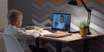 A young boy focused on a virtual class at his home desk, embracing modern education technology.