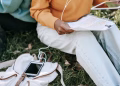 High angle of unrecognizable students in casual outfit sitting on lawn in park doing homework and using tablet