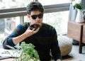 A man wearing sunglasses uses a smartphone's voice assistant in a cozy indoor setting.