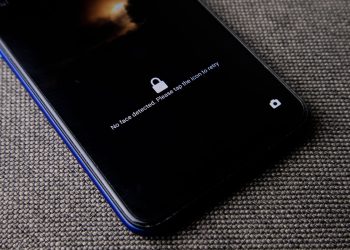 Mobile phone with no face detected message on lock screen on a textured fabric surface.