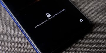 Mobile phone with no face detected message on lock screen on a textured fabric surface.
