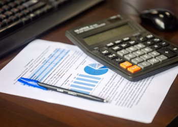 Desk with calculator, financial report, and pen, suggesting business analysis.