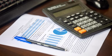 Desk with calculator, financial report, and pen, suggesting business analysis.