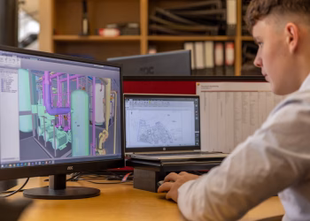 Engineer working with CAD software on dual monitors in an office setting.