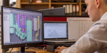 Engineer working with CAD software on dual monitors in an office setting.