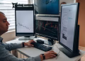 A professional in an office analyzing financial charts on multiple monitors, using advanced technology.