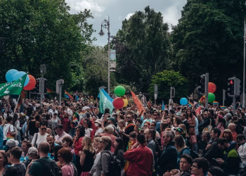 Large crowd gathered for an outdoor celebration with balloons and flags, enjoying a lively festival atmosphere.