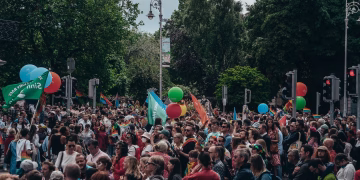 Large crowd gathered for an outdoor celebration with balloons and flags, enjoying a lively festival atmosphere.