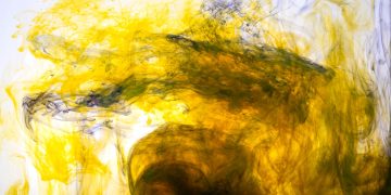 Dynamic abstract image of yellow ink swirling in water, creating mesmerising patterns.