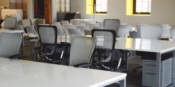 Spacious open office workspace with desks, chairs, and natural lighting.