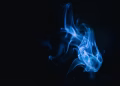 Blue smoke swirls creating abstract forms on a dark background, evoking a mysterious and dreamy atmosphere.