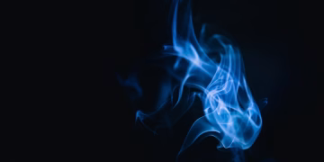 Blue smoke swirls creating abstract forms on a dark background, evoking a mysterious and dreamy atmosphere.