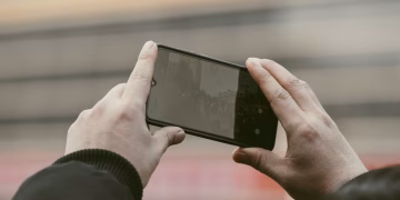 Close-up of hands using a smartphone to capture a photo outdoors.