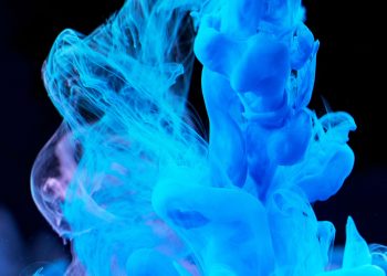 Dynamic blue ink swirls in water creating abstract shapes on a dark backdrop.