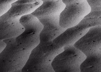 Black and white image highlighting the intricate shadow patterns of sand dunes. Natural abstract art.